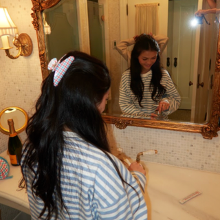Woman at a bathroom mirror wearing the FINNSUL Americana gingham claw clip in her hair
