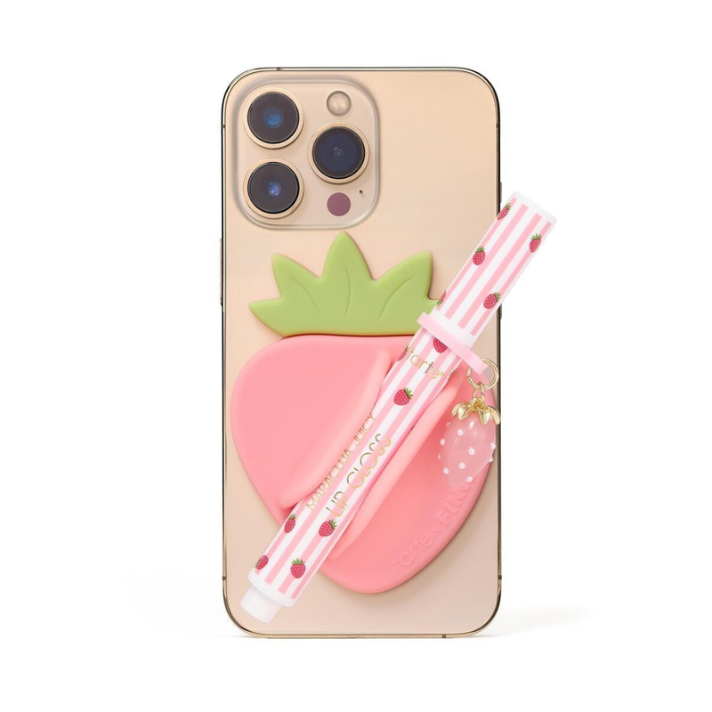A pink strawberry-themed phone case with a 3D strawberry design and a matching pink-and-white striped pen with a strawberry charm, shown on a light gold smartphone against a white background.
